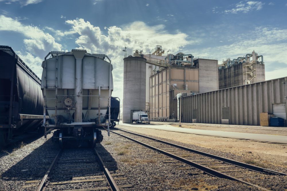 Desert landscape. Arizona heat beats down on industrial building and rail road track with cargo containers, silo and large facility in distance.