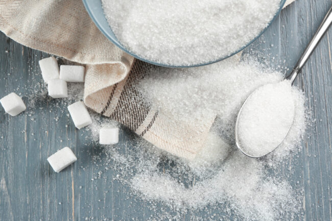 Bowl and spoon with sugar on wooden background