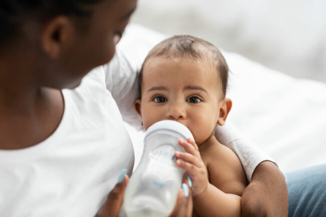 Baby drinks milk out of a bottle.