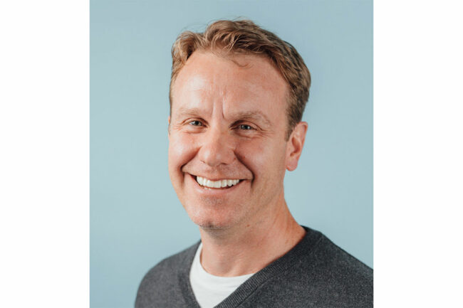 Andrew Burke, chief executive officer at Lotus Foods, smiles for the camera wearing a charcoal gray V-neck sweater. 