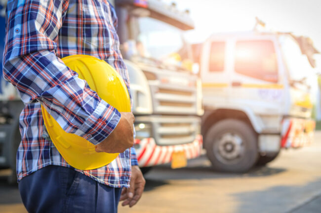 Man with construction hardhat by truck on sunny day. 