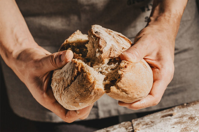 Baker cracking a fresh loaf of bread. 