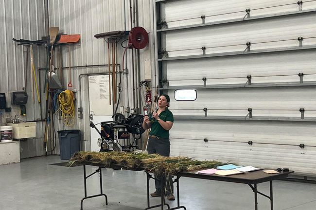 Clair Keene, an assistant professor of agronomy at North Dakota State University, shows 2024 Hard Spring & Durum Wheat Tour participants some of the crops grown in the Peace Garden state, such as barley and oats.
