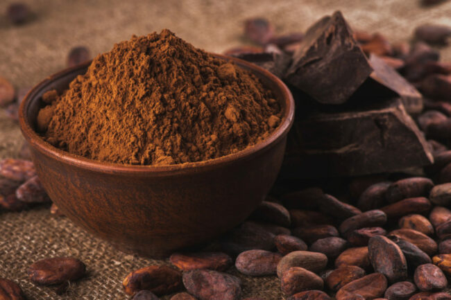 Bowl of cocoa powder next to cocoa beans. 