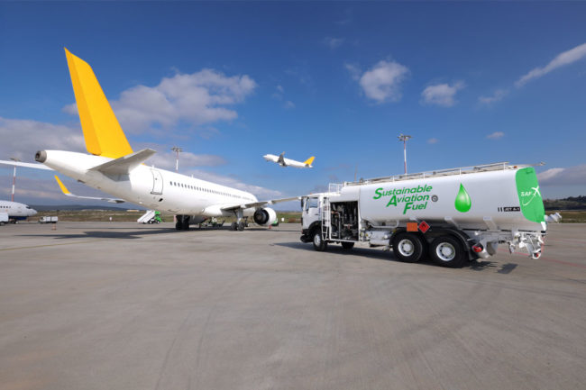 Sustainable aviation fuel truck next to airplane on tarmac. 