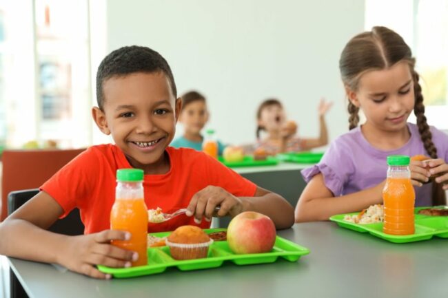 Child smiles while eating school lunch.