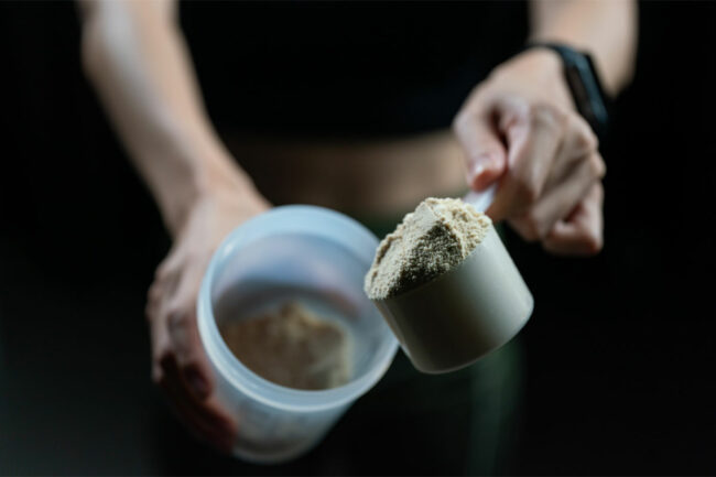 Woman putting protein powder in blender bottle.