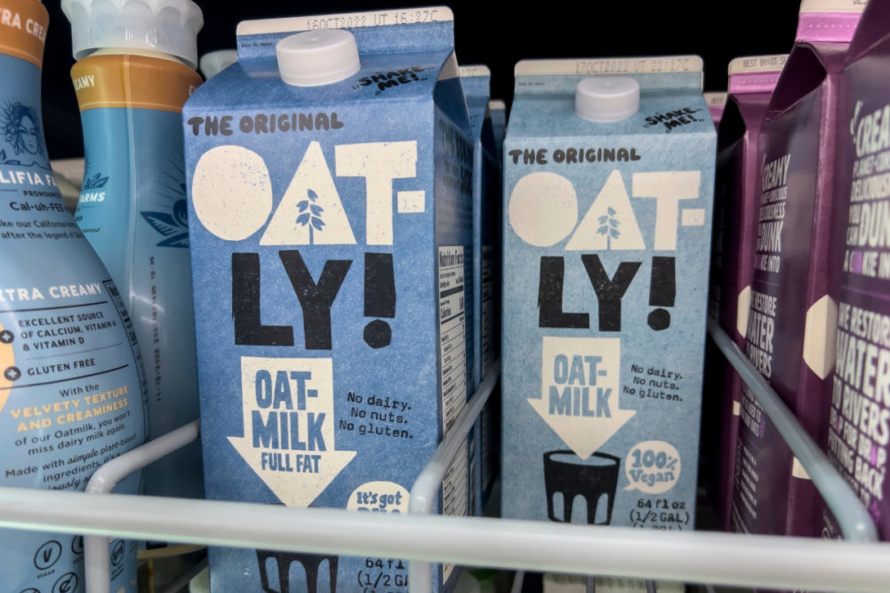 Two cartons of Oatly oat milk in grocery store fridge. 