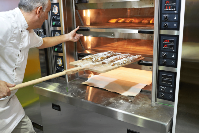 Baker placing bread in oven.