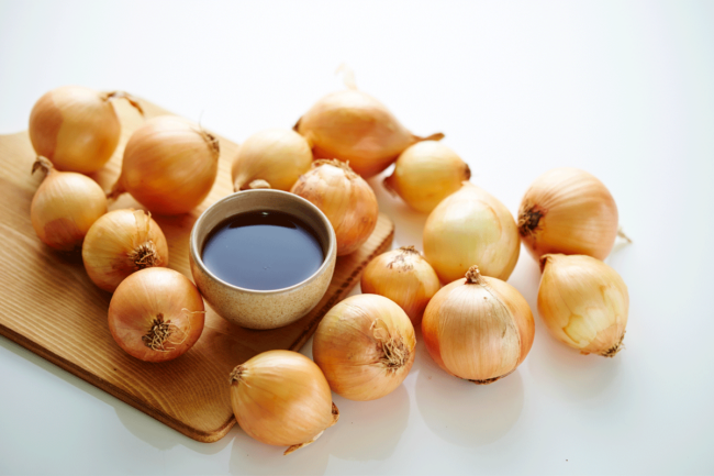 A dozen raw yellow onions on wooden cutting board. 